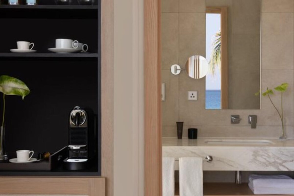 Un baño moderno con un espejo grande, encimera de mármol y un estante con artículos de aseo.