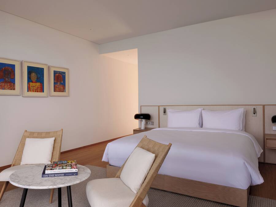 Una habitación de hotel con una cama, dos sillas, una mesita y tres cuadros enmarcados en la pared.