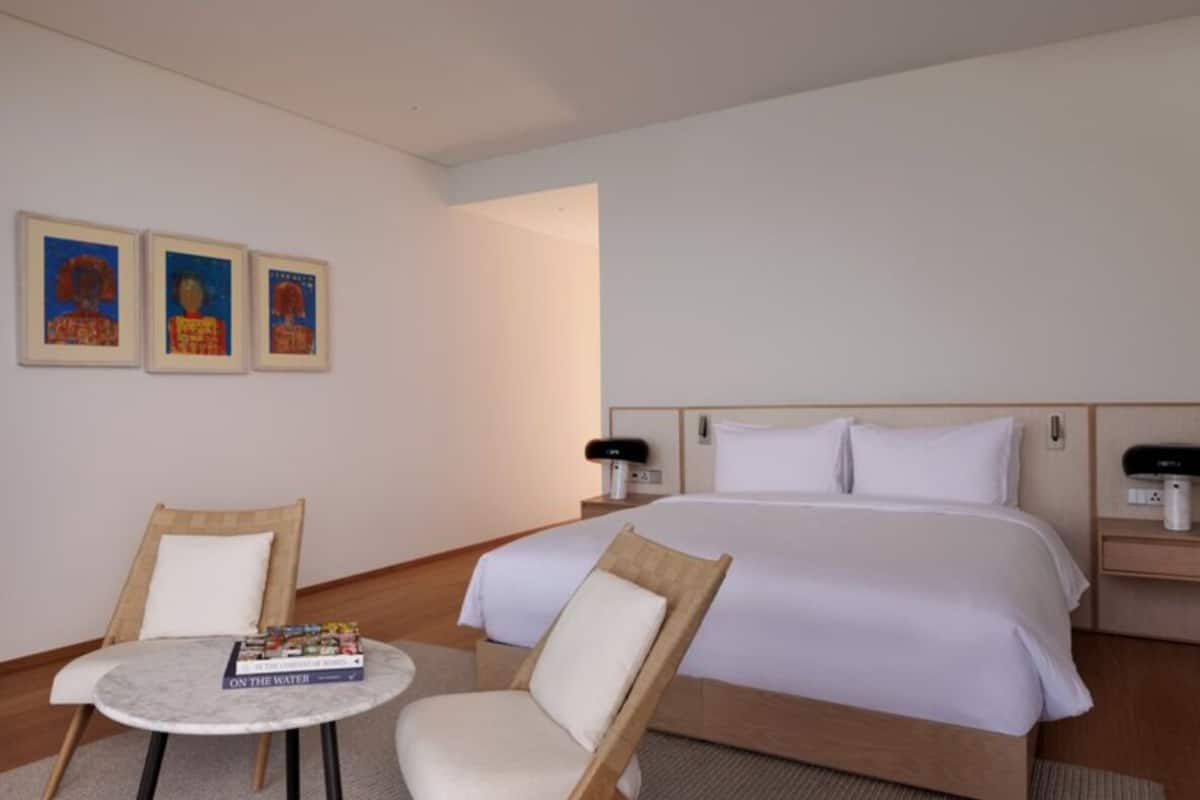 A hotel room with a bed, two chairs, a small table, and three framed pictures on the wall.