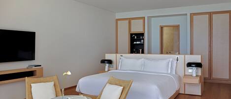 A hotel room with a large bed, a TV, a small table with chairs, and a bedside table with a lamp.