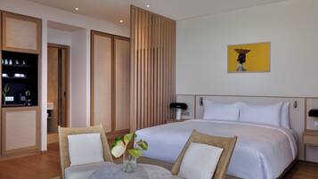 Habitación de hotel con una cama grande, dos sillas, una mesita con un florero y un cuadro en la pared.