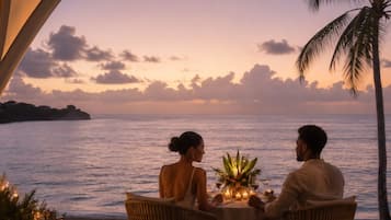 A couple dining at a table with a view of the ocean and palm trees.