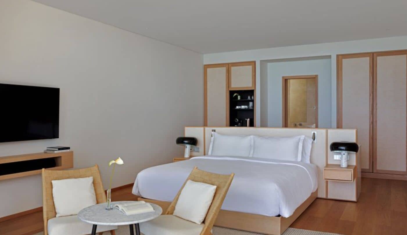 A hotel room with a bed, two bedside tables, a TV, a small table with chairs, and a mirror.