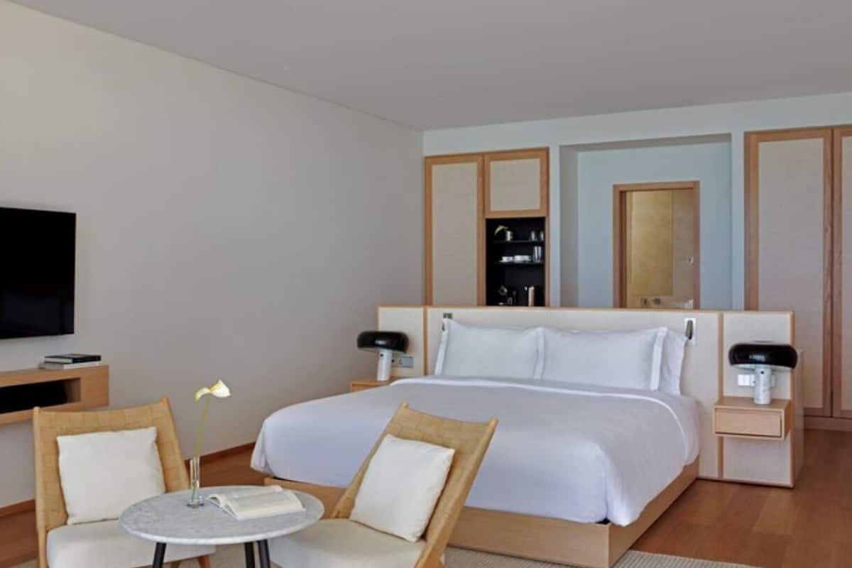 A hotel room with a bed, two bedside tables, a TV, a small table with chairs, and a mirror.