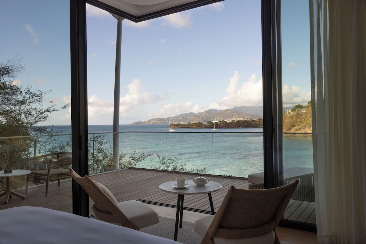 A balcony with a view of the sea and mountains, furnished with a table and chairs.