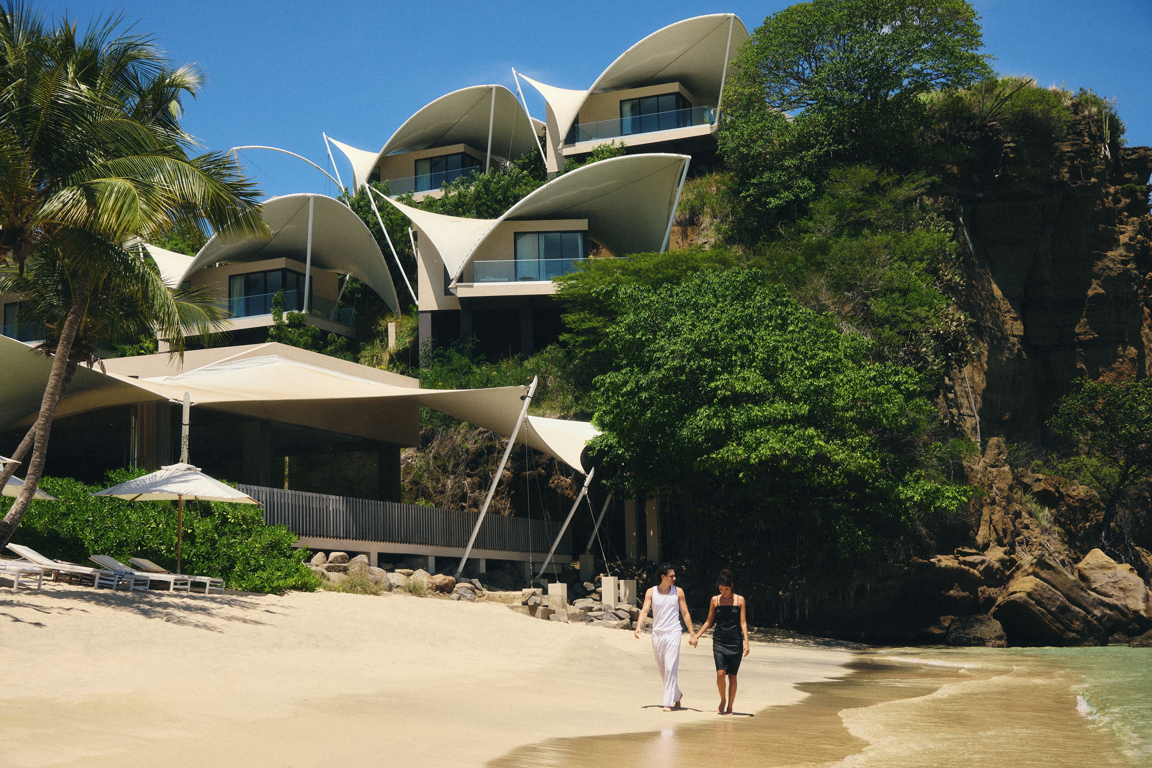 A beachfront hotel with multiple levels of balconies, palm trees, and a sandy beach.