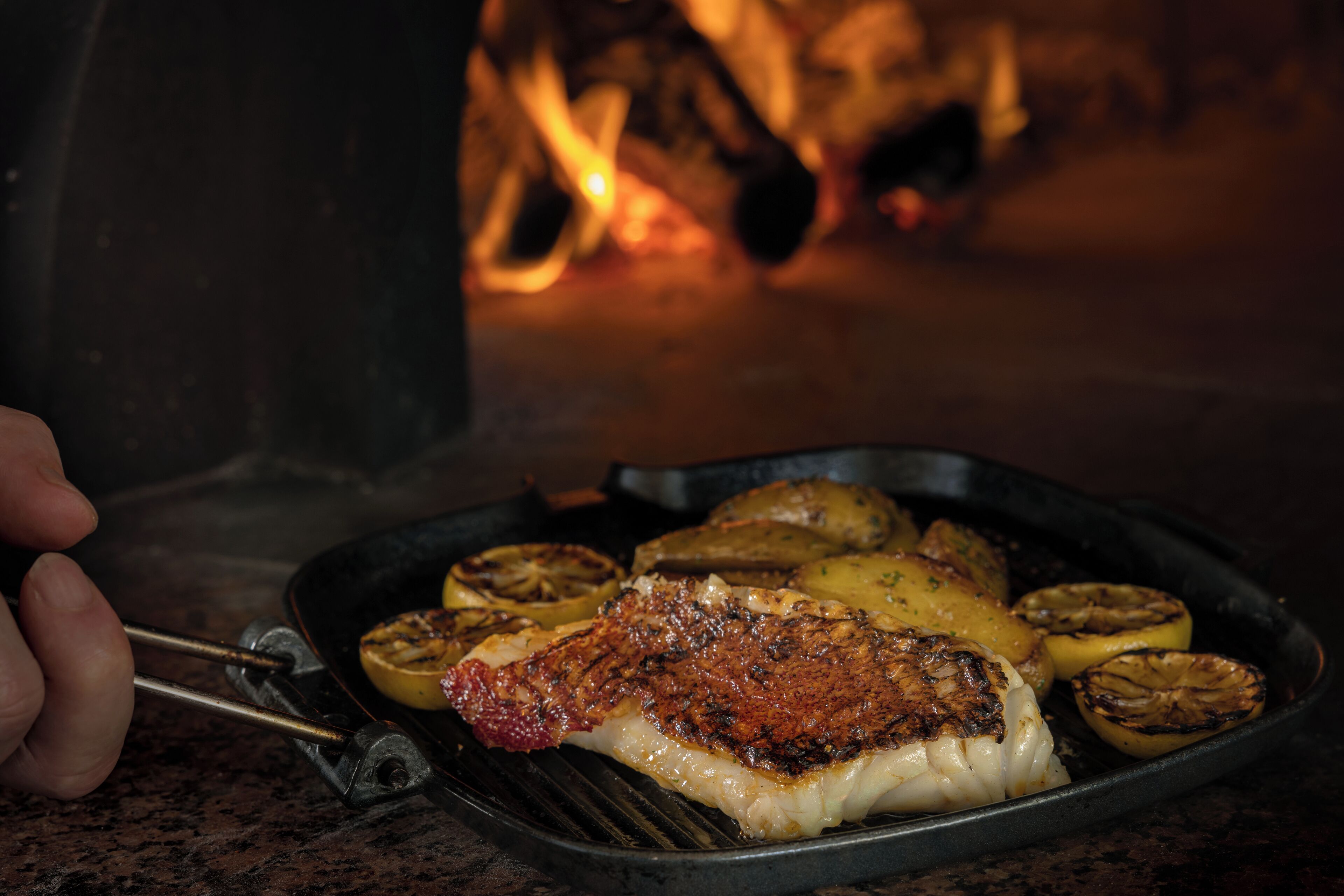 A grilled fish fillet with lemon slices and potatoes on a grill pan.