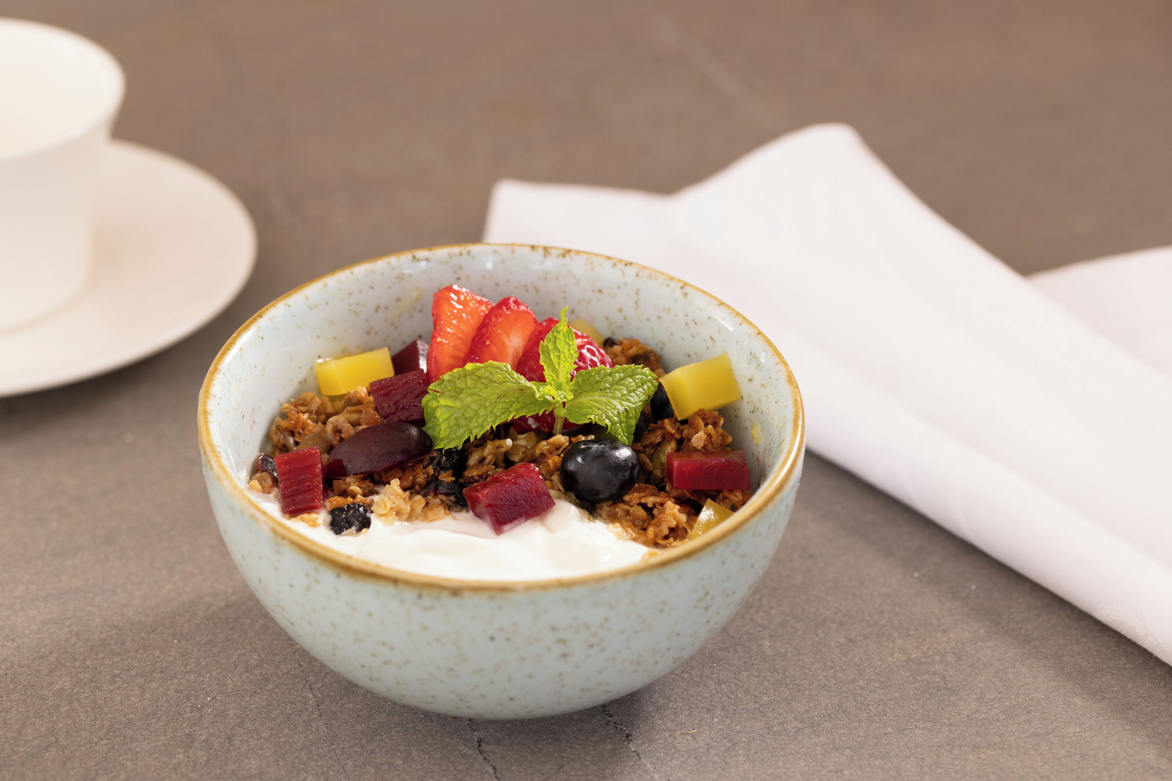 En skål yoghurt med granola og blandede bær på et bord.