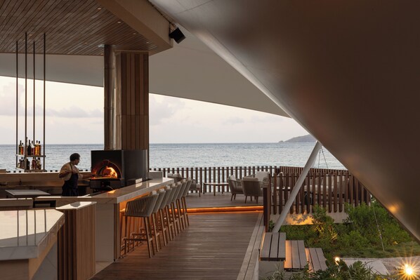Zona de bar al aire libre con vistas al mar, terraza de madera y asientos.
