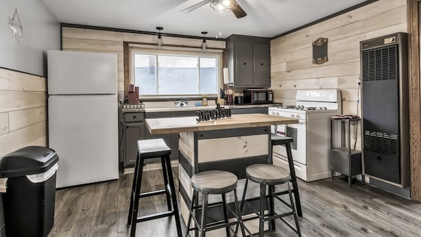 Cocina moderna con una isla central, taburetes de bar, ventilador de techo y paneles de madera.