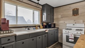 Una cocina con armarios grises, una estufa blanca y una ventana con persianas.