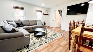 A modern living room with a sectional sofa, a coffee table, and a dining table with chairs. - Cozy Colonial in Downtown Westfield, NY (Westfield)
