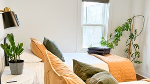 A bedroom with two beds, a bedside table with a lamp, a potted plant, and a window with a view. - Cozy Colonial in Downtown Westfield, NY (Westfield)