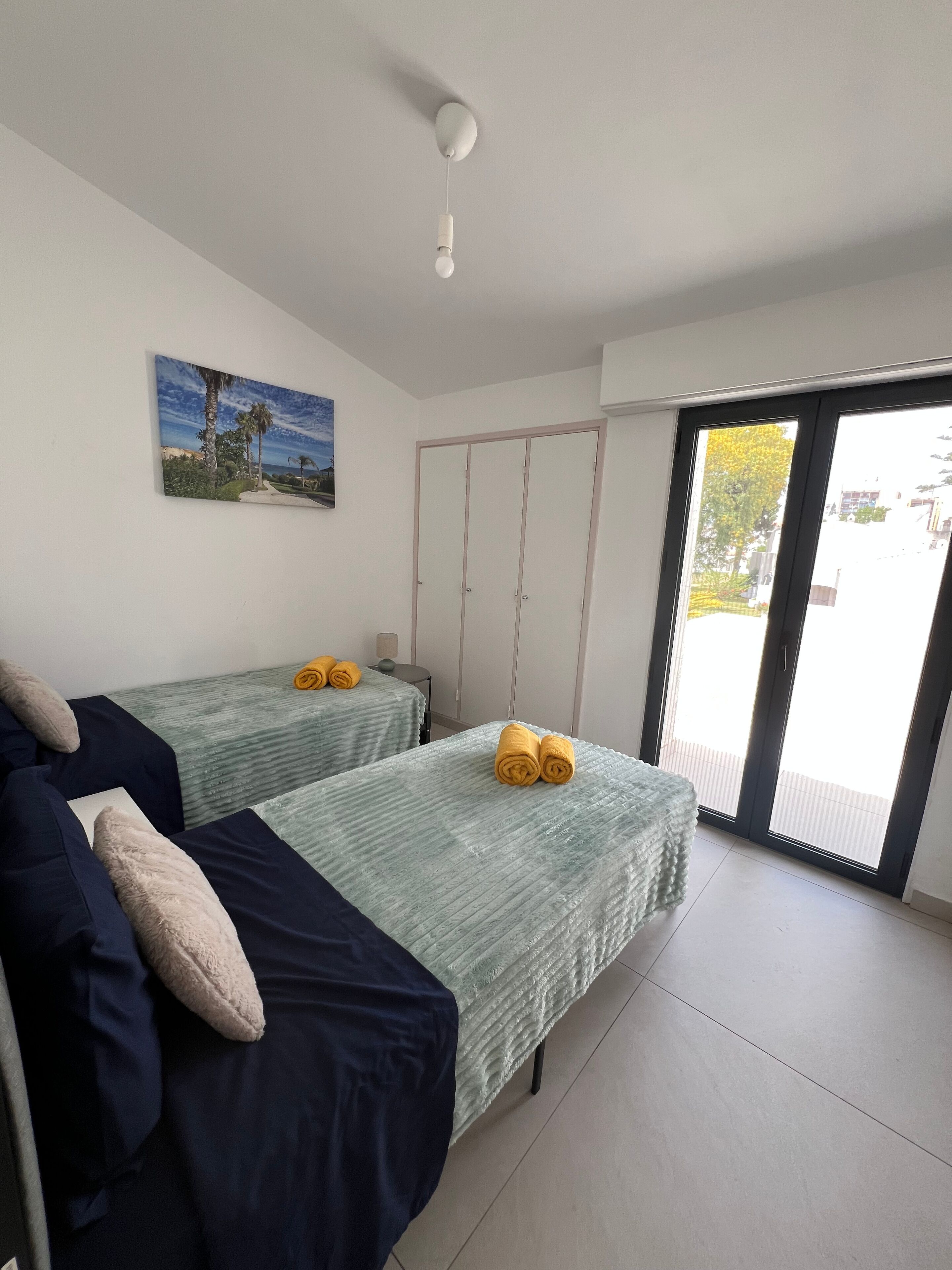 Un dormitorio con dos camas, un cuadro, un armario y una puerta corrediza a un balcón.