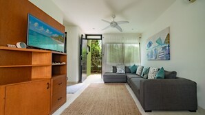 A living room with a grey sofa, a wooden cabinet, a flat-screen TV, and a ceiling fan. - Tranquilidad 3 Bedroom Home At El Cielo (Playa del Carmen)