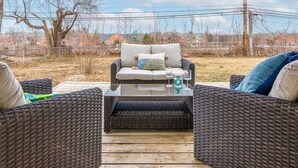 Eine Sitzgruppe im Freien aus Rattan mit gepolstertem Sofa und zwei Stühlen, einem Glastisch mit zwei Weingläsern und einer Flasche, und Blick auf Häuser im Hintergrund.