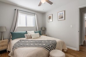 A bedroom with a bed, bedside tables, a window with curtains, a ceiling fan, and two framed pictures on the wall. - World Cup Home Base 30 Day Stay Netherlands Camp (Kansas City)