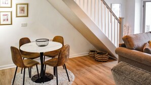 Un área de comedor con una mesa redonda, cuatro sillas y un tapete blanco. Se ve una escalera con baranda de madera al fondo.