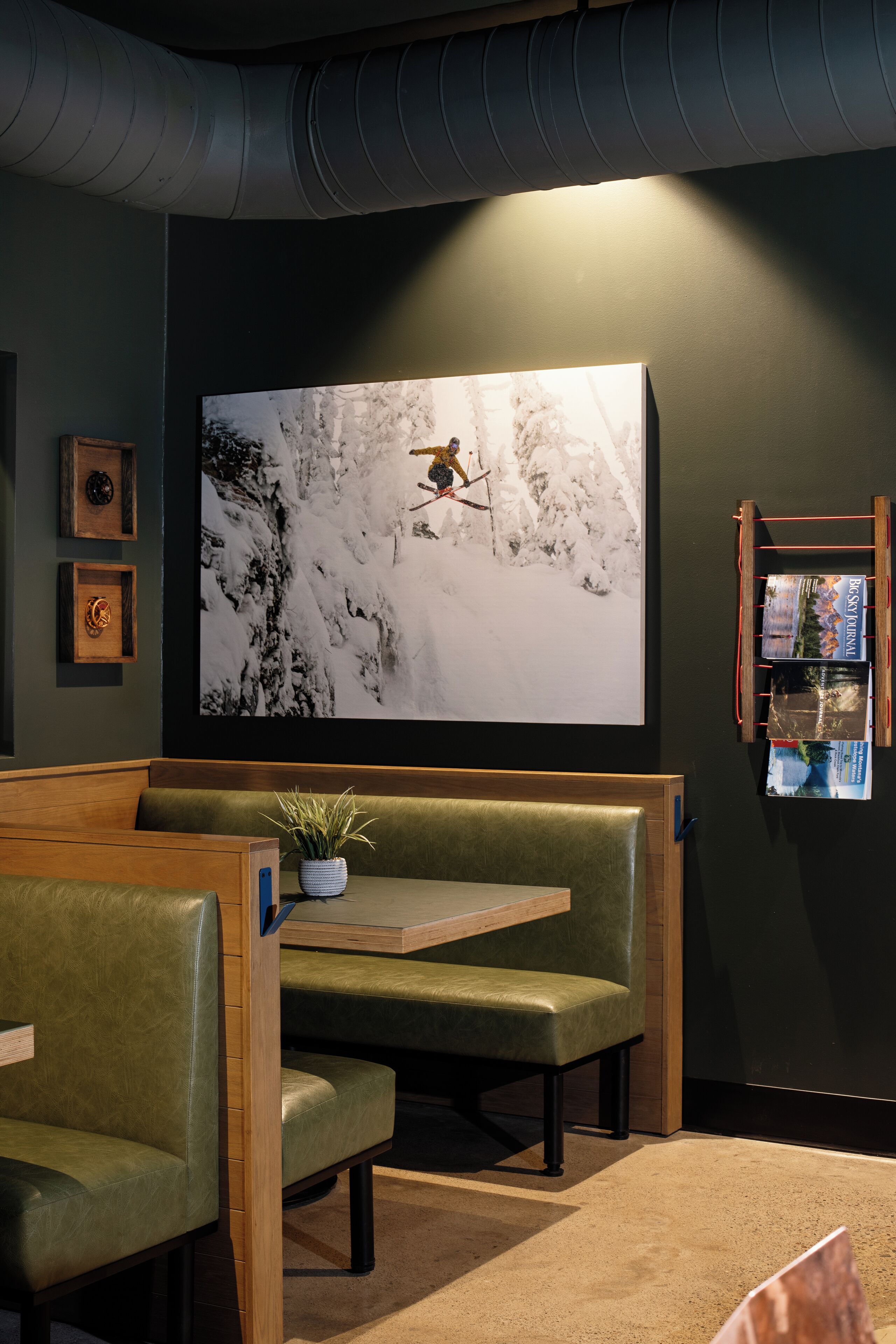 Un interior moderno con un televisor de pantalla grande montado en la pared que muestra un paisaje nevado, un rincón con banca de madera y una mesita con una planta en maceta.