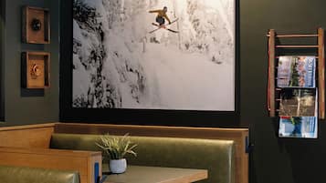 Un interior moderno con un televisor de pantalla grande montado en la pared que muestra un paisaje nevado, un rincón con banca de madera y una mesita con una planta en maceta.