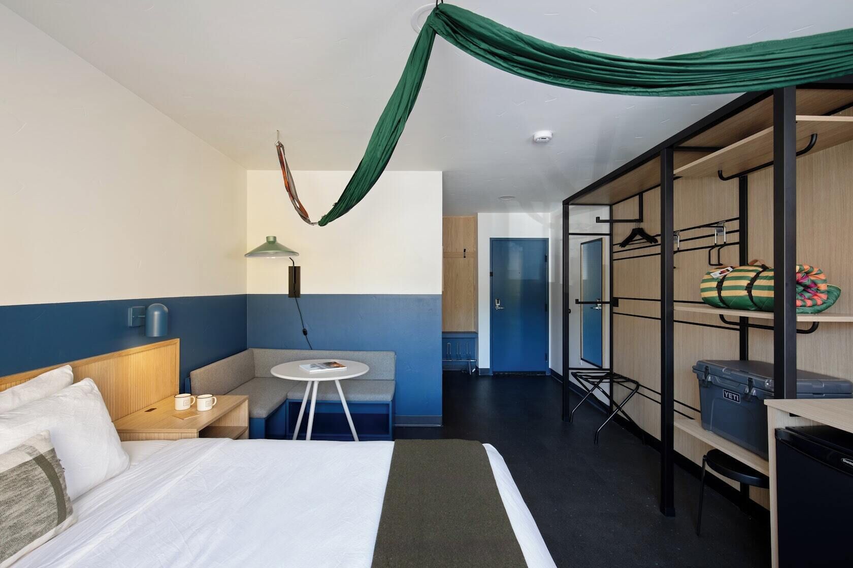 Een hotelkamer met een bed, een zithoek met een tafel, een kledingkast en een groene stoffen gordijn.