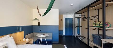 Een hotelkamer met een bed, een zithoek met een tafel, een kledingkast en een groene stoffen gordijn.