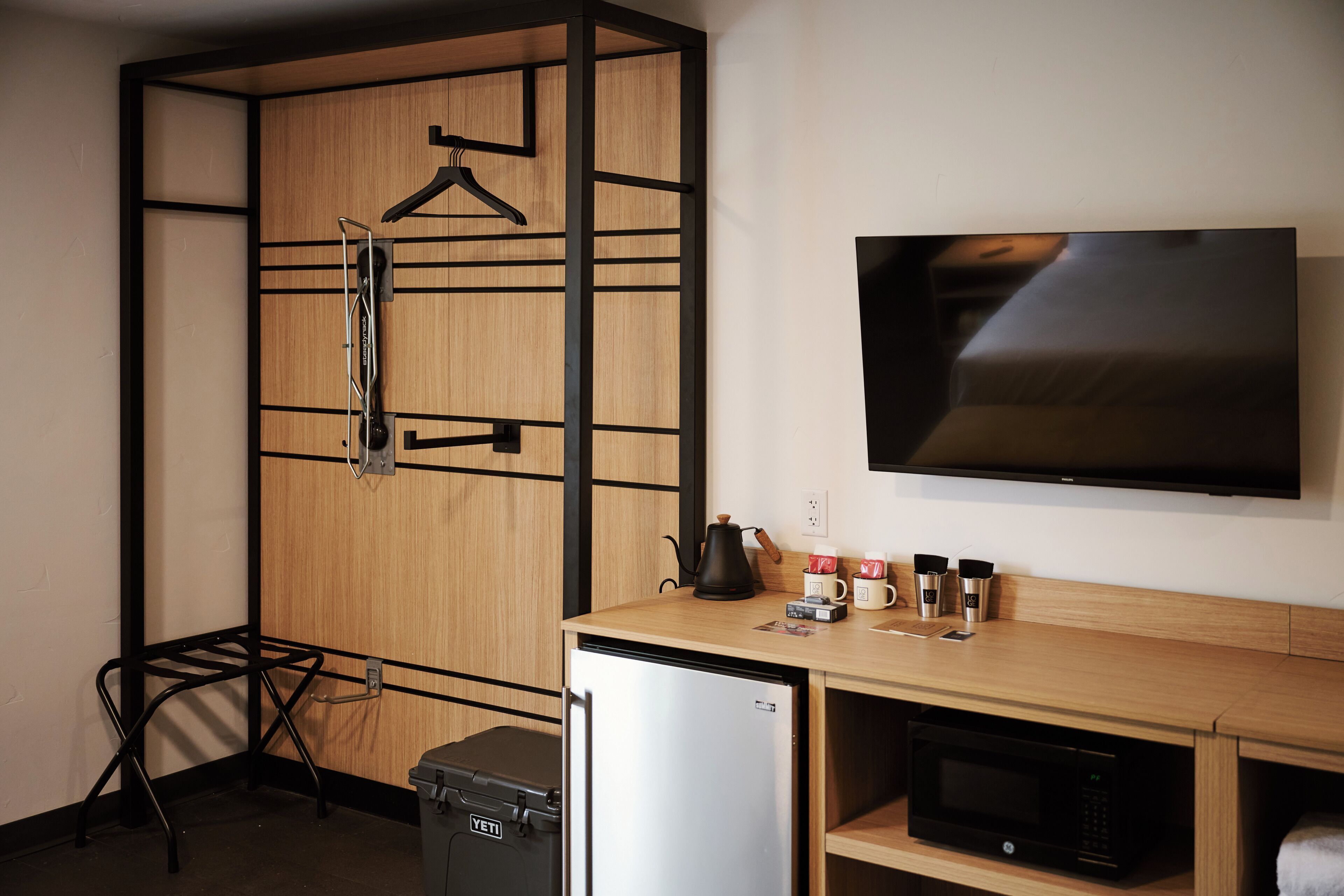 Une chambre compacte comprenant une armoire en bois, un petit réfrigérateur, un four à micro-ondes, une machine à café et un téléviseur fixé au mur.