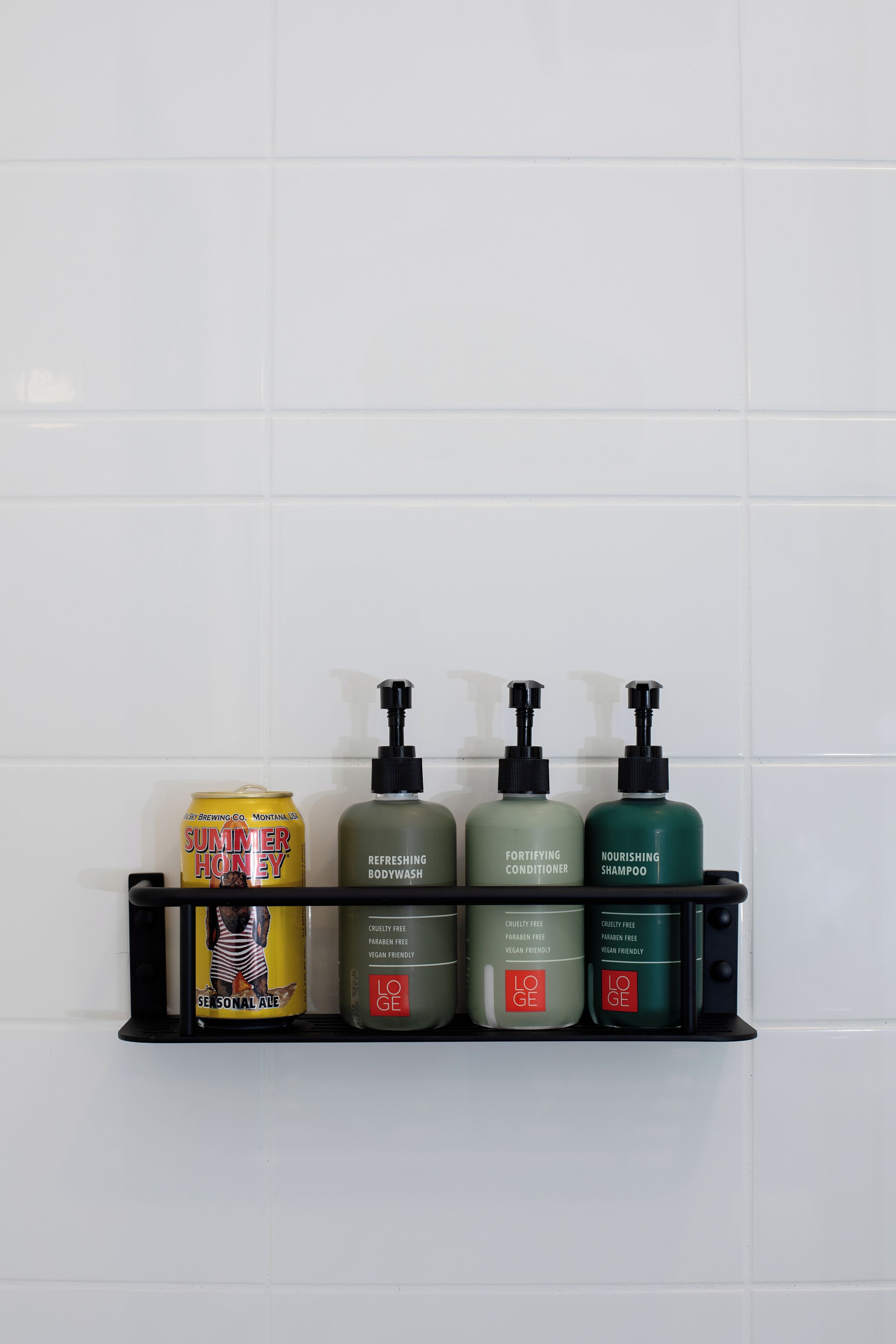 A bathroom shelf with a can of Summer Honey seasonal ale, refreshing body wash, fortifying conditioner, and nourishing shampoo.