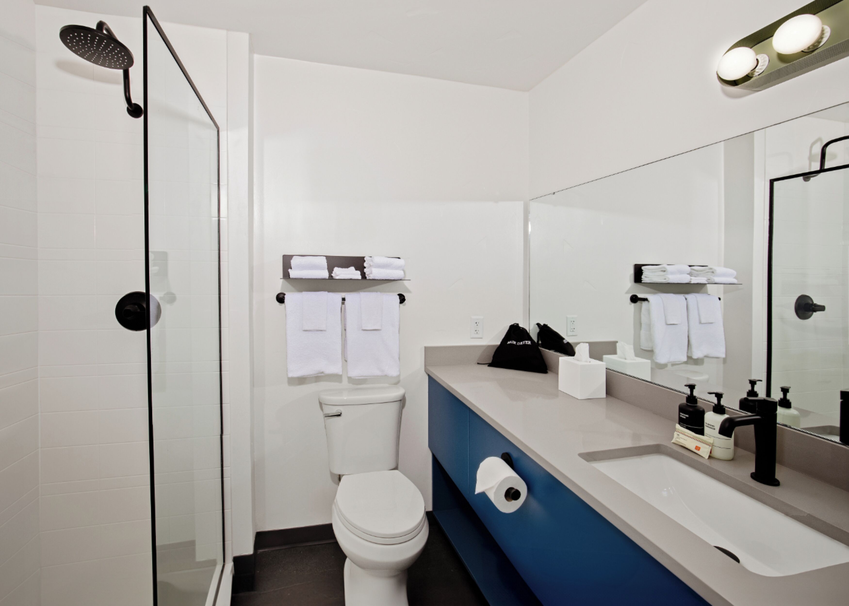 Un baño moderno con cabina de ducha de vidrio, inodoro, lavamanos con espejo y toallas ordenadas.