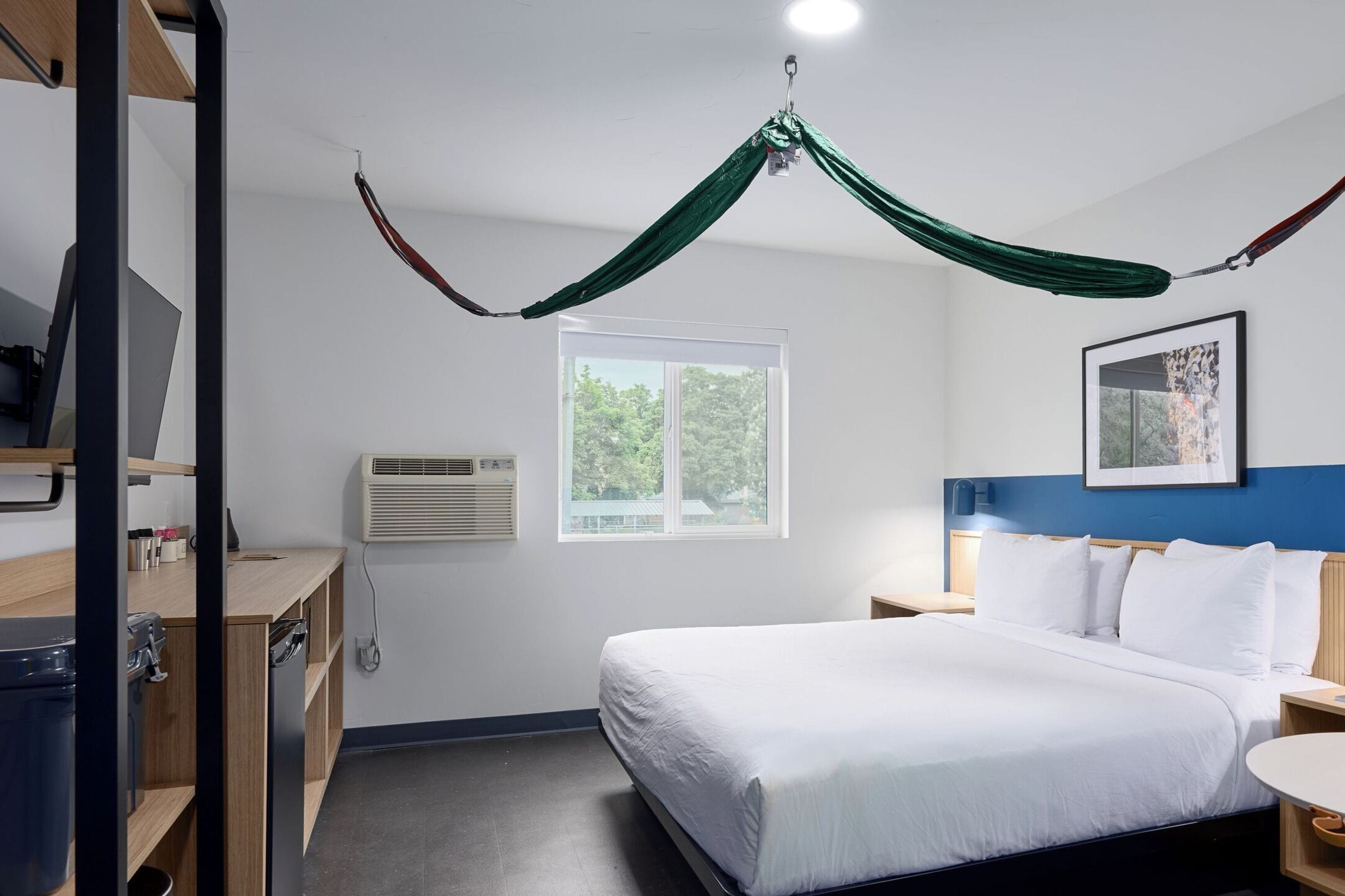 Ett hotellrum med en säng, ett skrivbord, en stol, ett fönster och ett grönt sänghimmel.