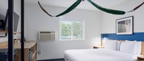 Habitación de hotel con cama, escritorio, silla, ventana y dosel verde.
