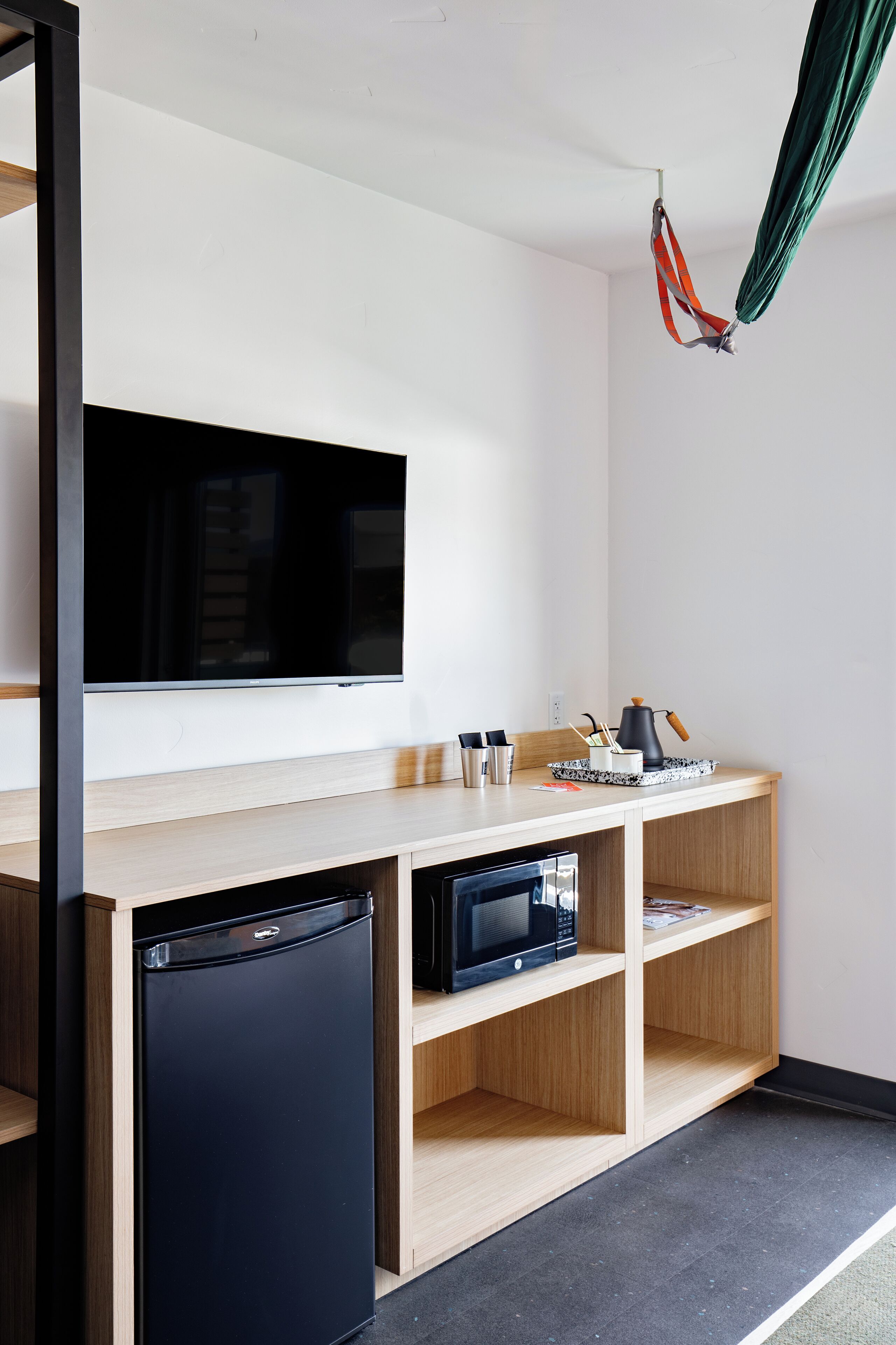 Une chambre moderne équipée d’un téléviseur à écran plat, d’un petit réfrigérateur, d’un four à micro-ondes et d’un comptoir en bois sur lequel se trouve un plateau contenant des ustensiles.
