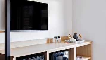Une chambre moderne équipée d’un téléviseur à écran plat, d’un petit réfrigérateur, d’un four à micro-ondes et d’un comptoir en bois sur lequel se trouve un plateau contenant des ustensiles.