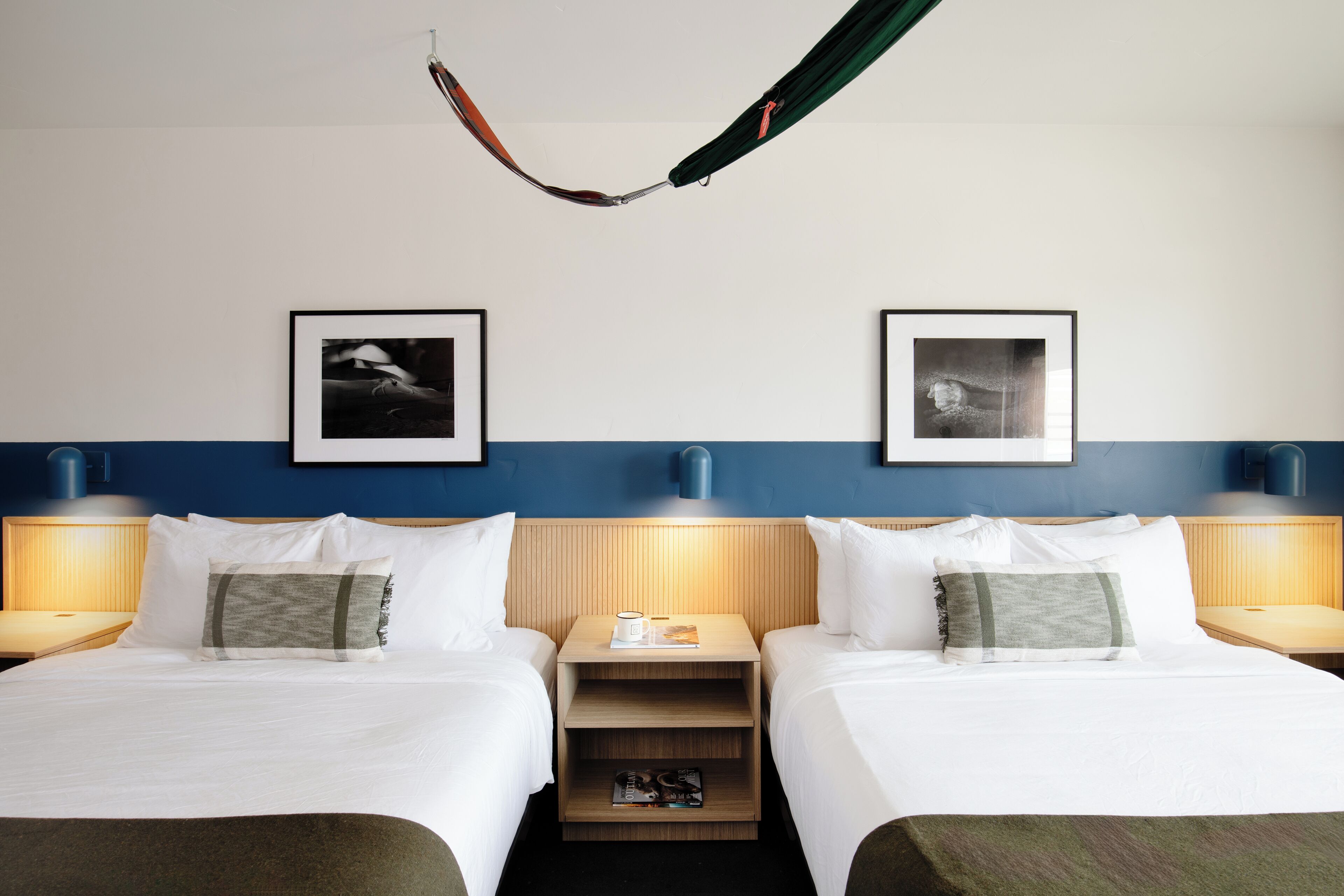Ein Hotelzimmer mit zwei Betten, einer Hängematte, gerahmten Bildern an der Wand und Nachttischlampen.