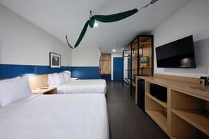 Quarto de hotel com duas camas, uma escrivaninha, televisão e chuveiro.