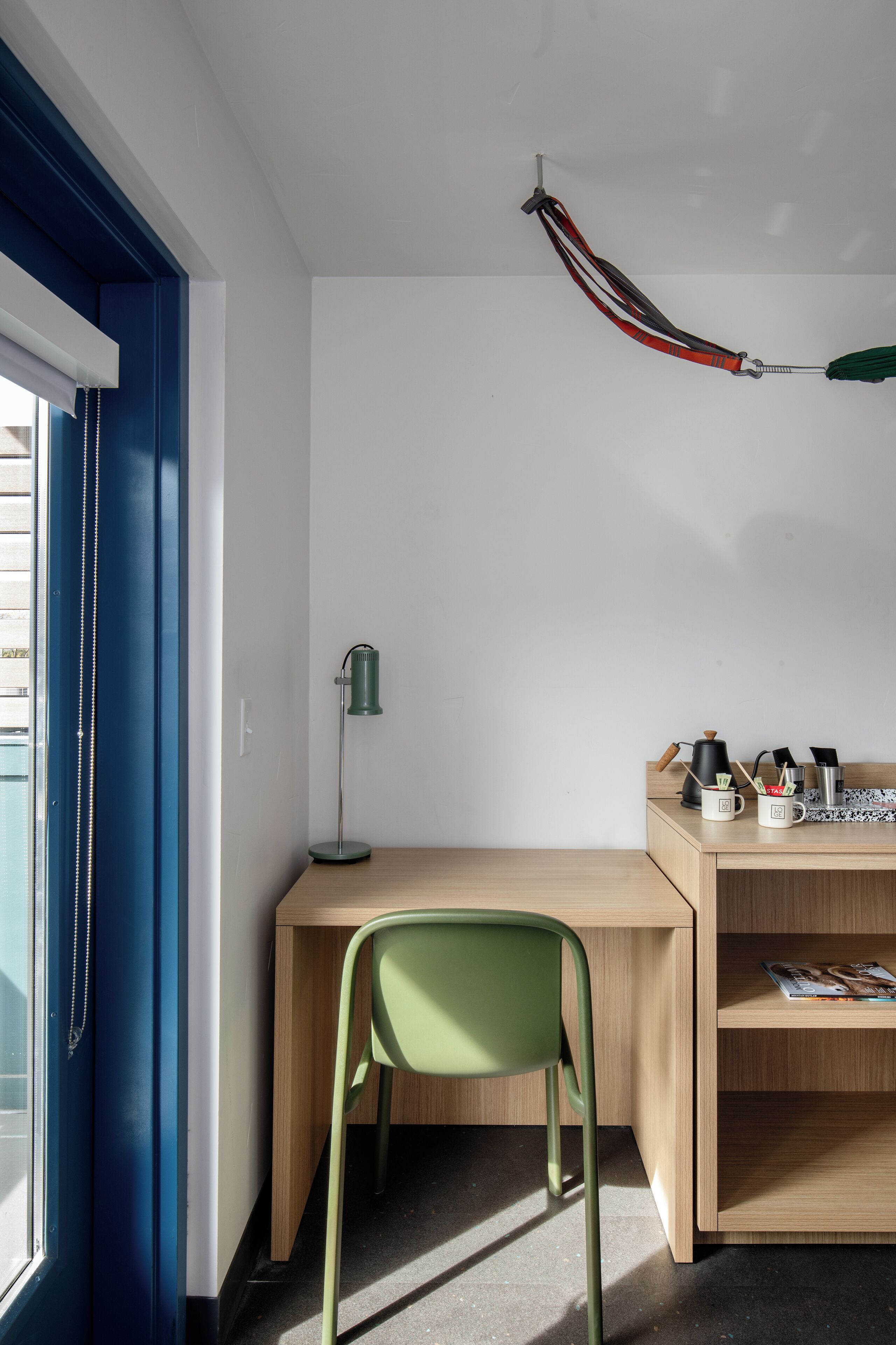 Een kamer met een bureau, stoel, lamp en een raam met jaloezieën.