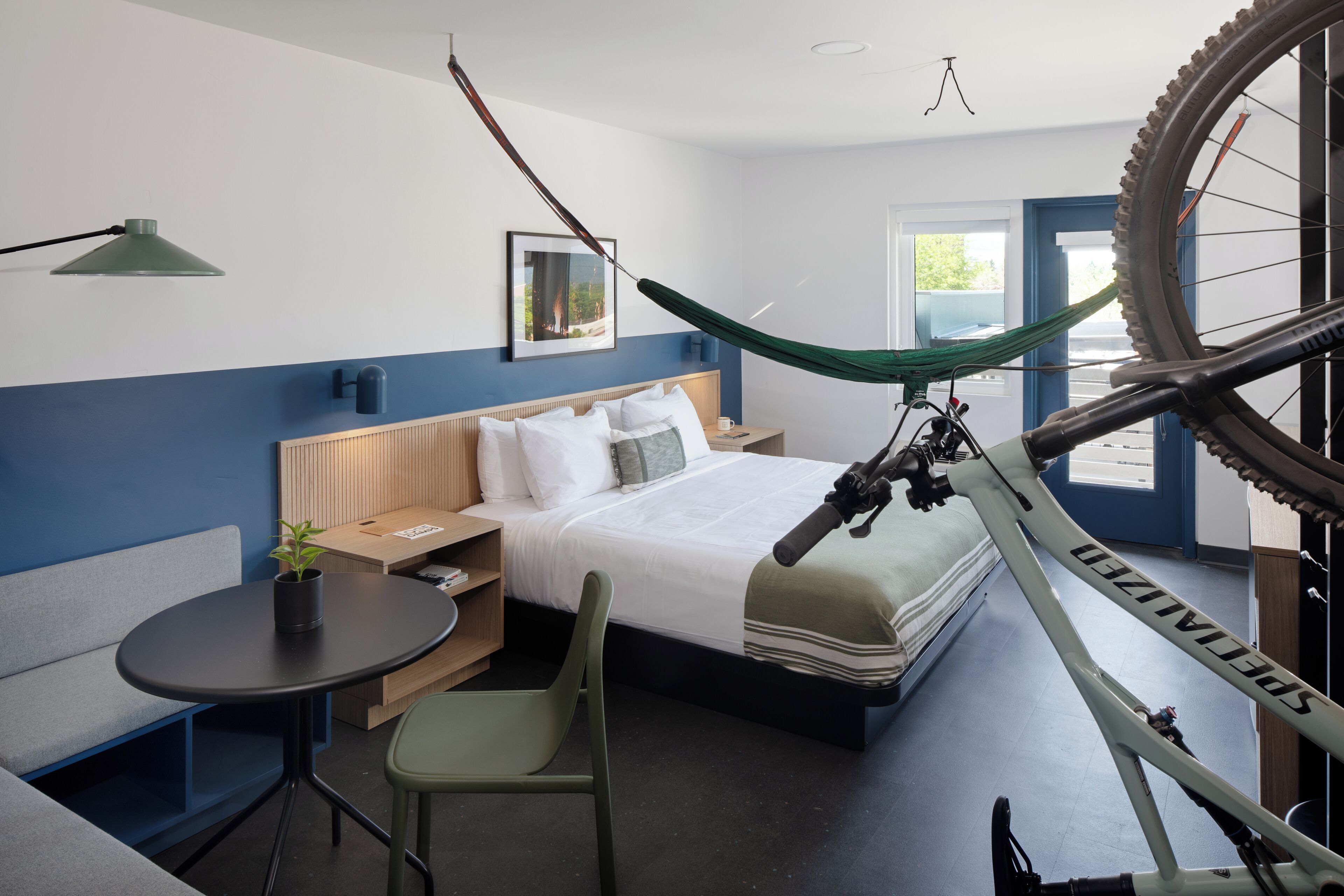 A modern hotel room with a bed, a desk, a chair, a bicycle, and a window.