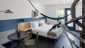 A modern hotel room with a bed, a desk, a chair, a bicycle, and a window.