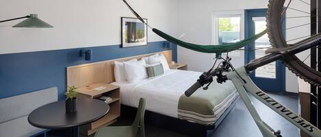 Una habitación de hotel moderna con cama, escritorio, silla, bicicleta y ventana.