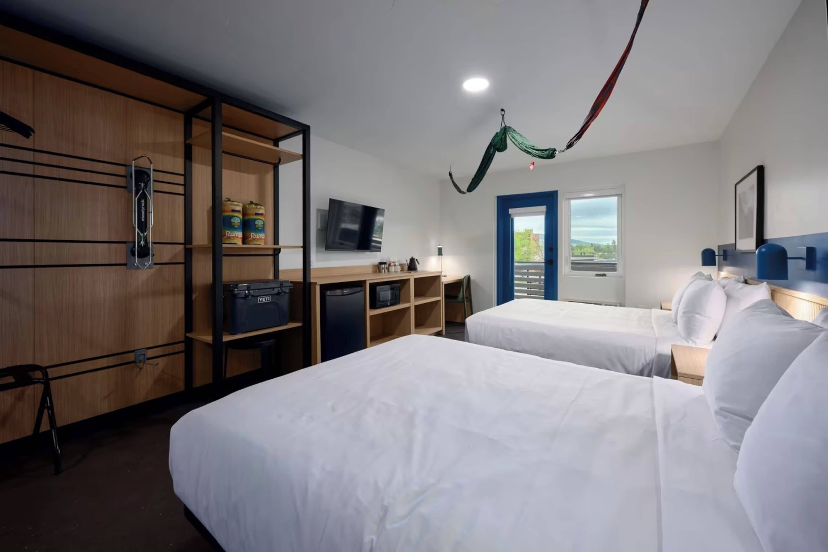 A hotel room with two beds, a desk with a chair, a TV, and a window with a view.