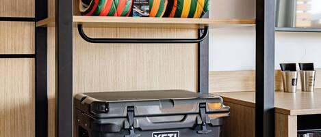 Una habitación pequeña con un estante de madera, un taburete negro y una maleta gris con la etiqueta 'YETI'.