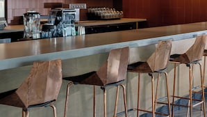 Eine Bar mit Hockern, hängenden Pendelleuchten und Regalen mit Gläsern und Tassen.