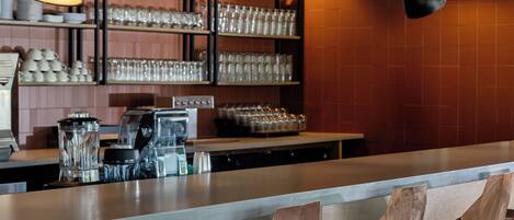 A bar area with stools, hanging pendant lights, and shelves with glasses and cups.