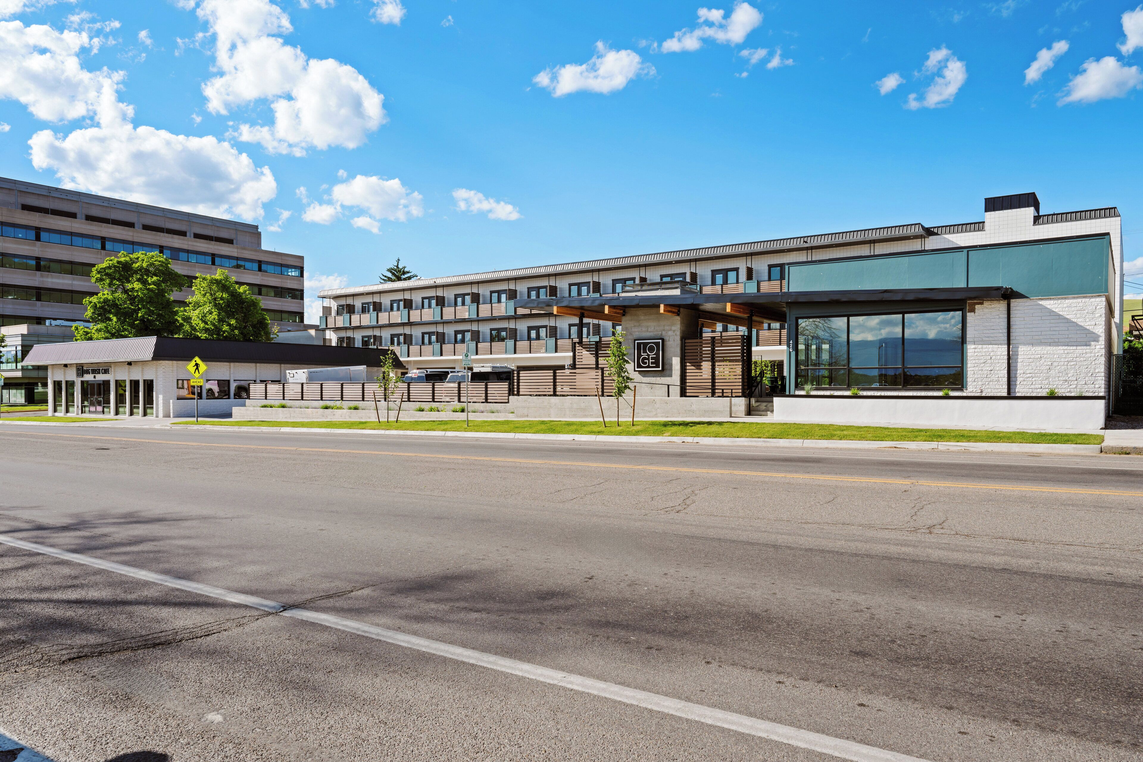 A modern hotel with a large glass facade, a pedestrian crossing sign, and a parking lot.