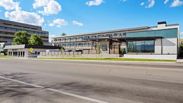 A modern hotel with a large glass facade, a pedestrian crossing sign, and a parking lot.