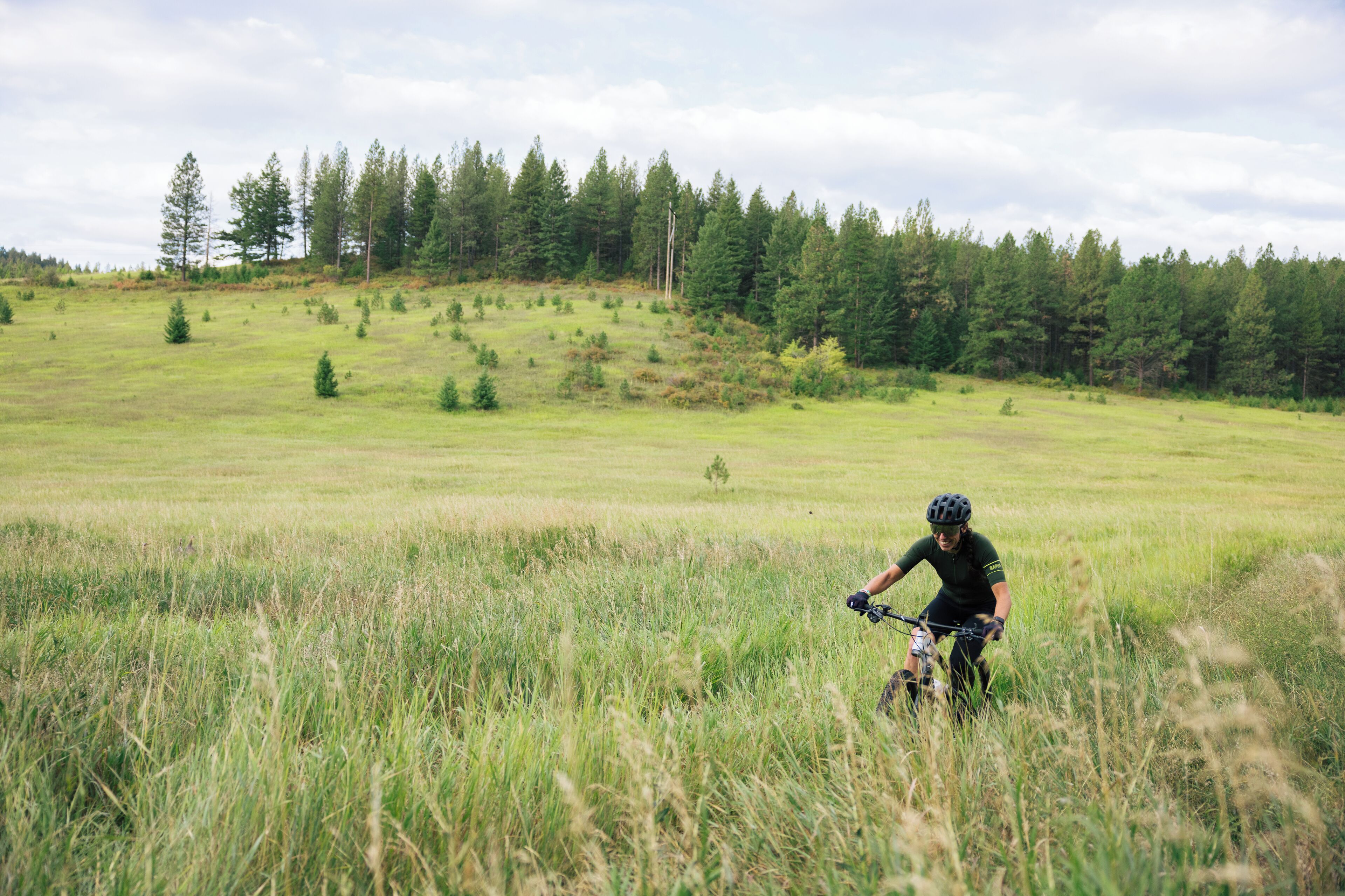 Una persona montando una bicicleta de montaña en un campo cubierto de hierba, con árboles al fondo.