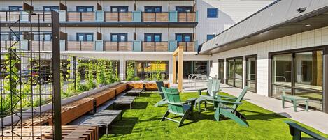 A modern building with a rooftop garden, outdoor seating area, and large windows.