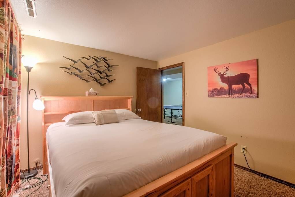A neatly made bed in a room with a wooden headboard, a wall-mounted abstract art piece, and a framed picture of a deer.