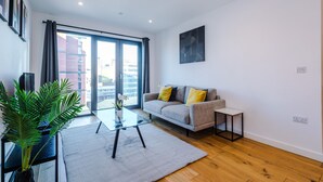 Una sala de estar moderna con un sofá, una mesa de centro de vidrio, una planta en maceta y vistas amplias a través de grandes ventanales.