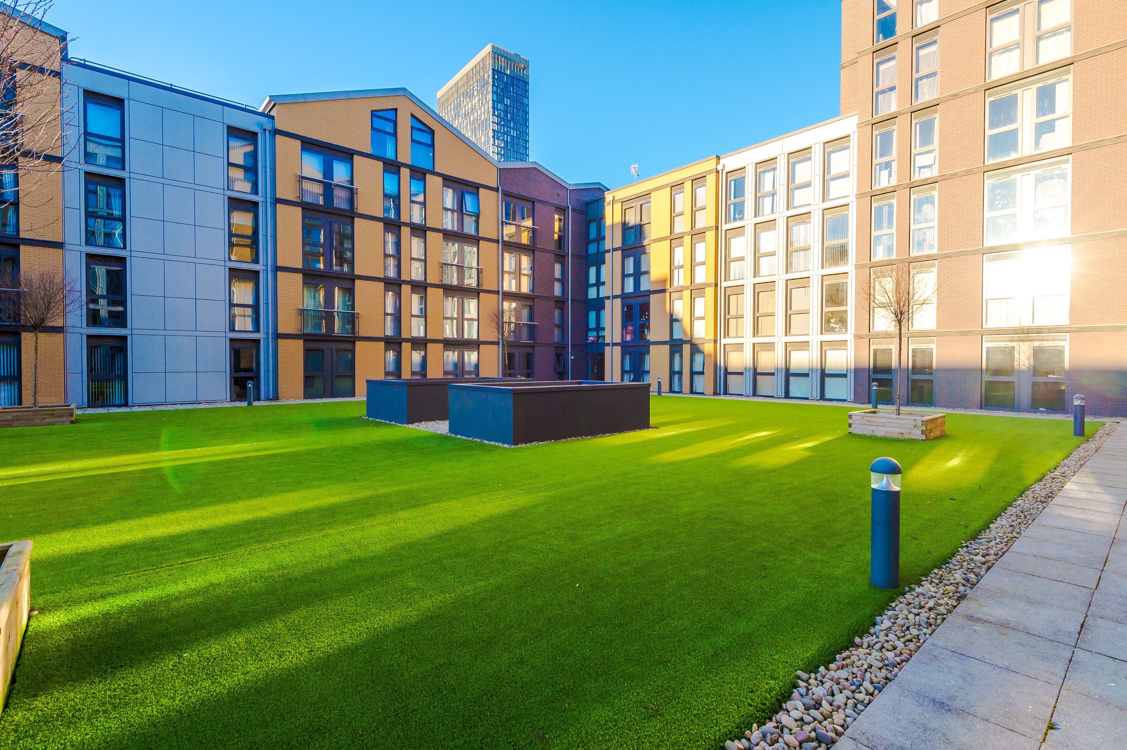 A courtyard with a well-maintained lawn, a seating area, and modern buildings with multiple windows and balconies.